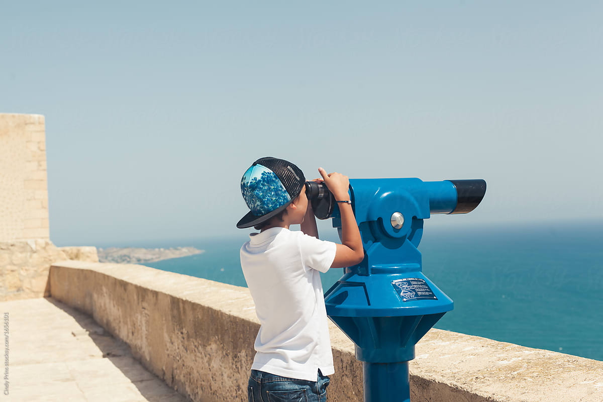 Boy looking at the ocean through a binocular telescope