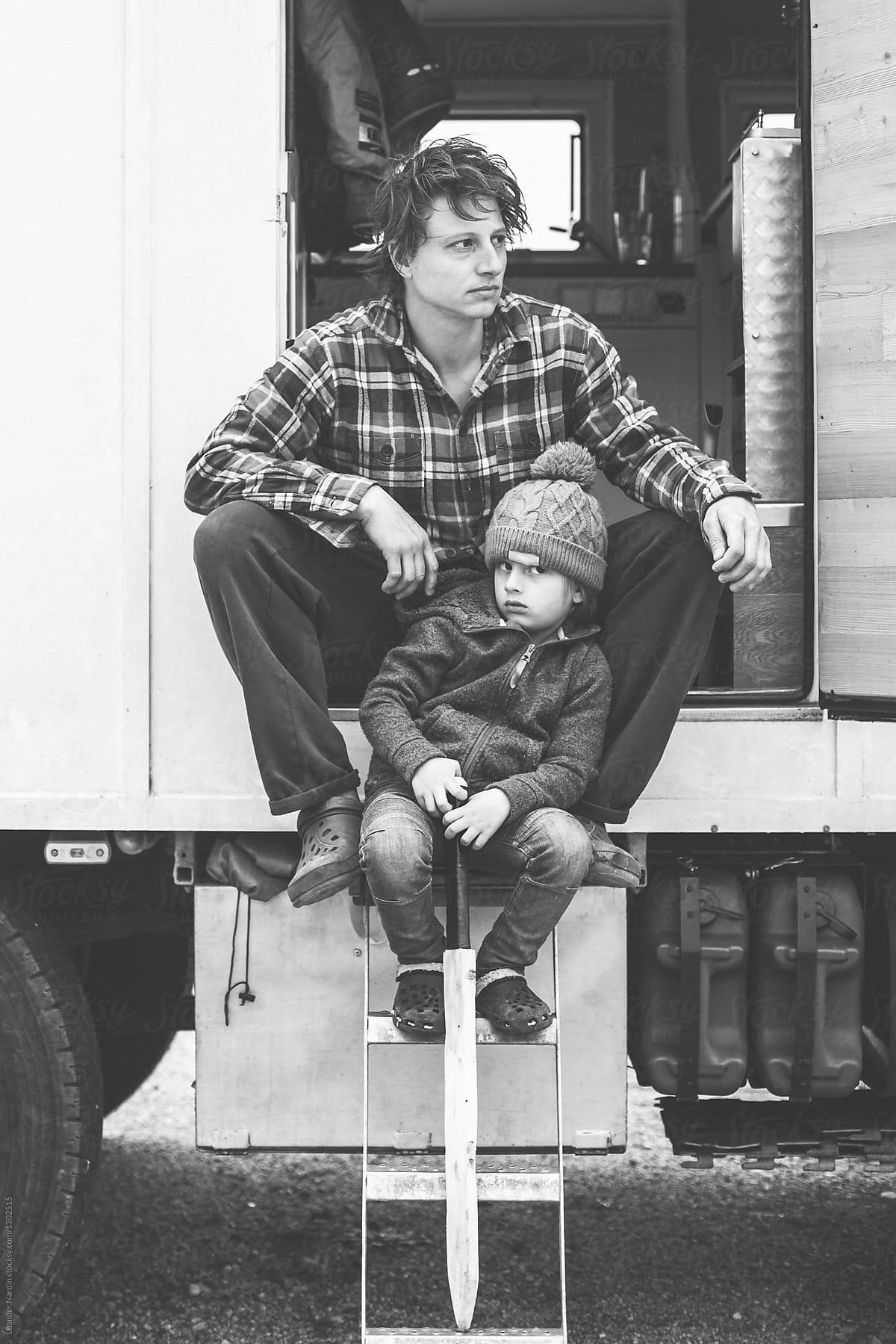father and son with wooden sword sitting on entrance stairs of a camping truck
