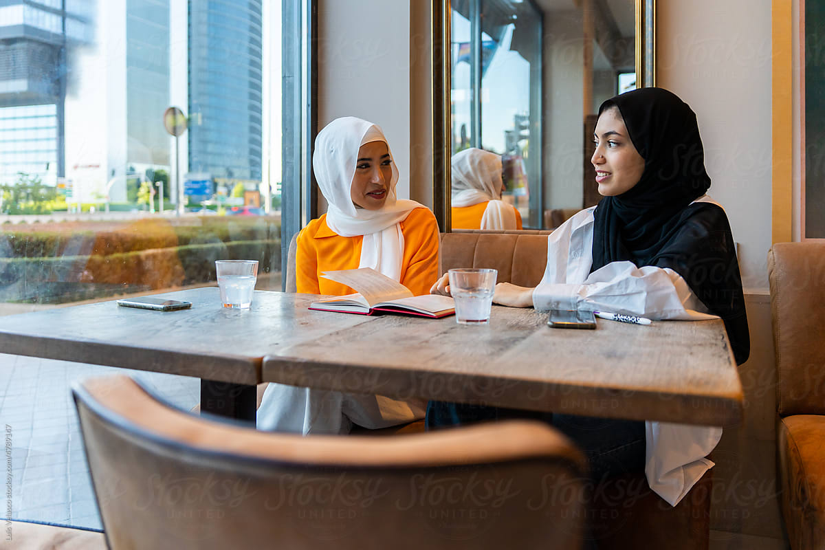 Two Muslim Girls Talking In A Urban Cafe.