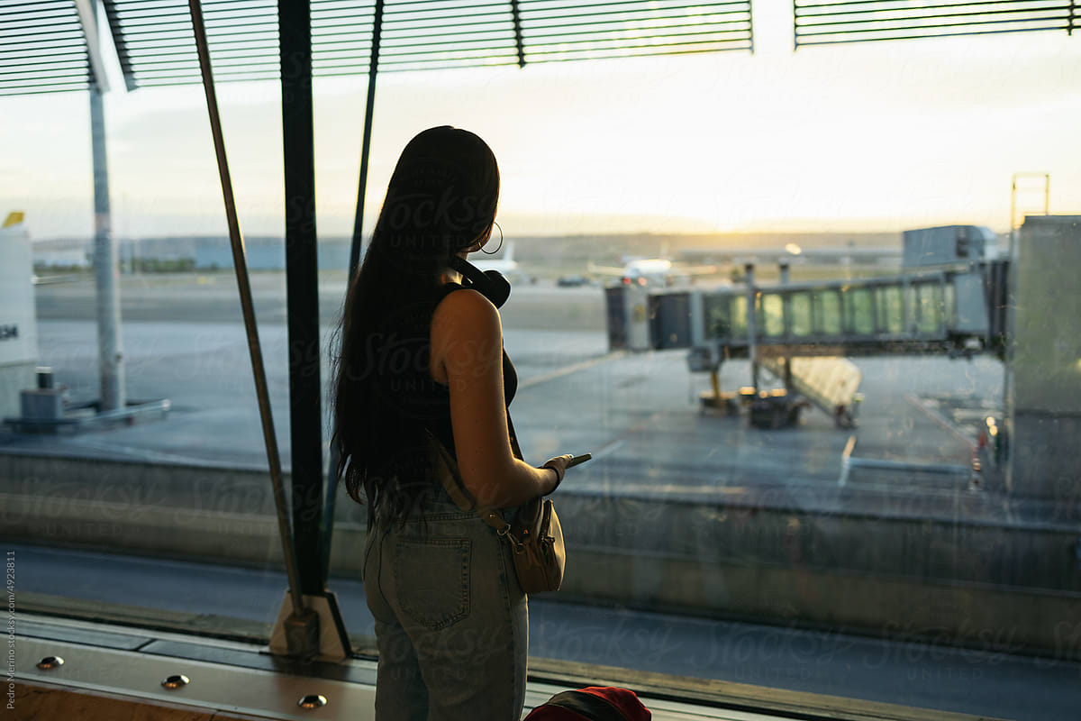 Woman at the airport looking at planes through the glass window