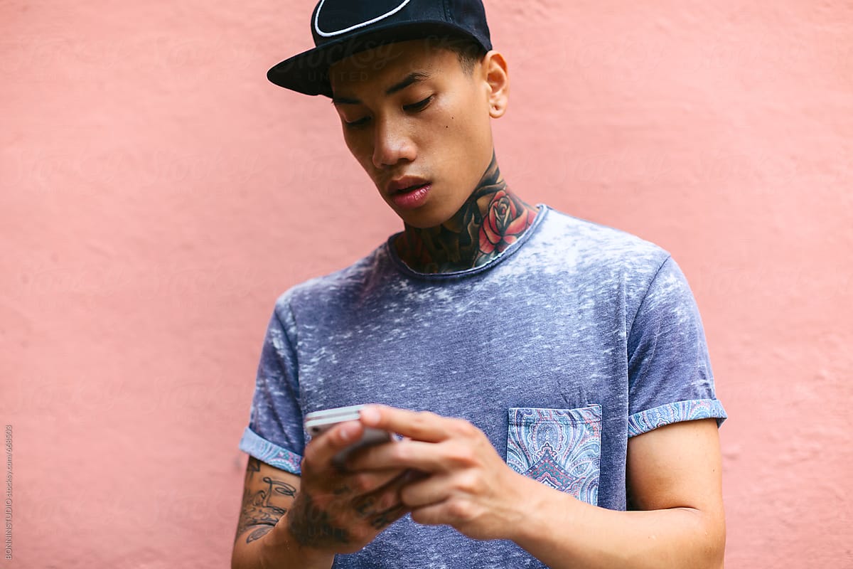Portrait of an asian tattooed man using his smartphone in front of a colorful wall.