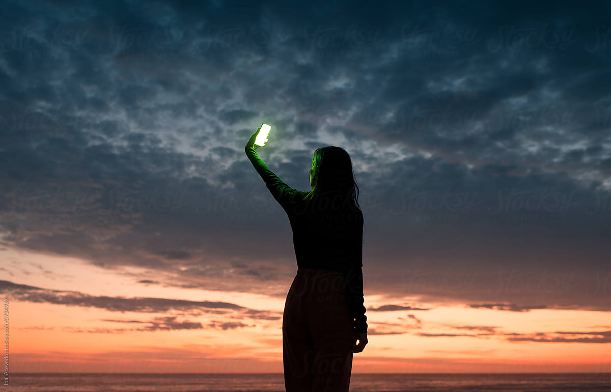 Woman holding up luminous phone during sea sunset
