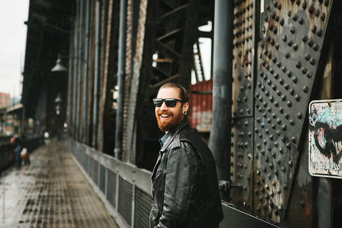Hip smiling man with his hair in a bun standing on a bridge