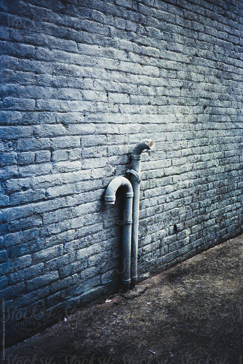 Drain pipes against a blue painted brick wall
