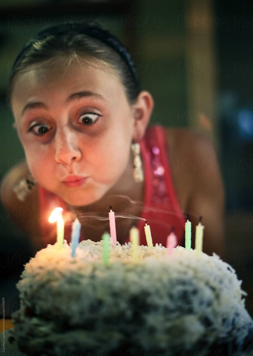 Girl with wide eyes and puffy cheeks blowing out birthday candles on a cake
