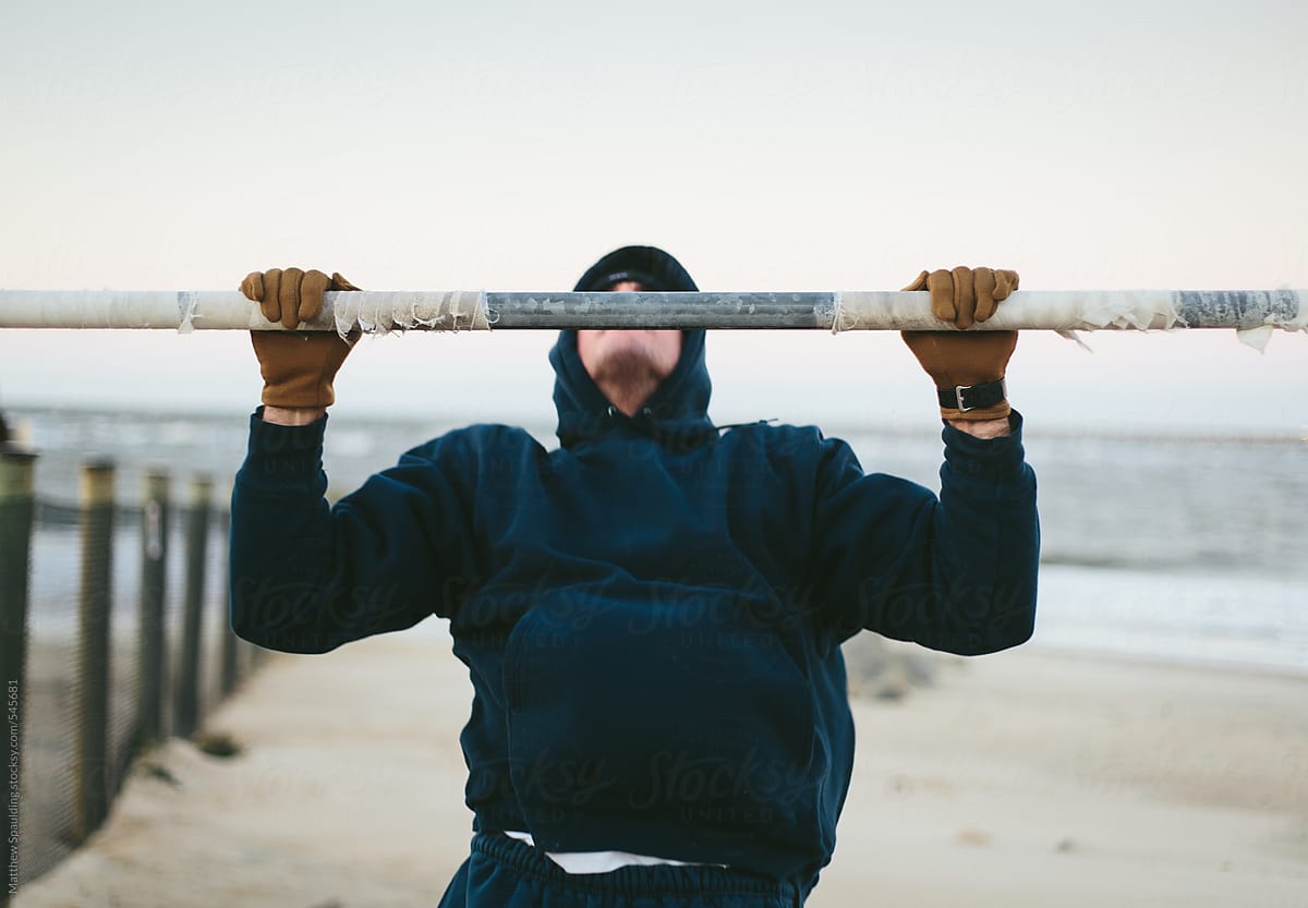 Man in sweat shirt doing pullup exercises on beach outdoors