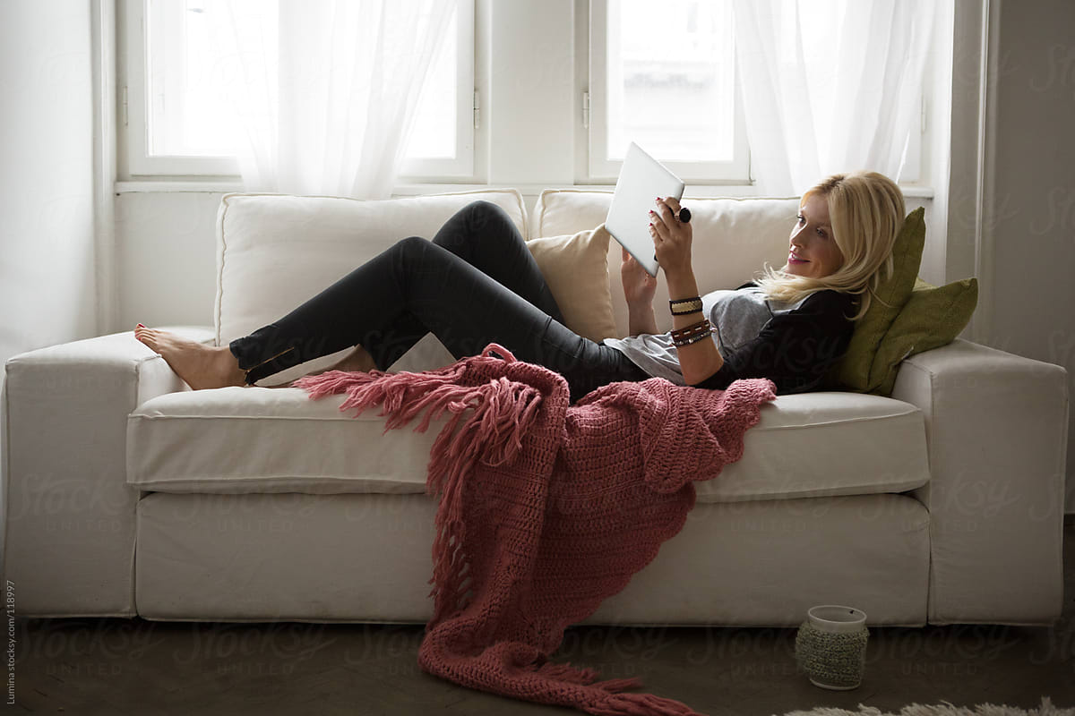 Woman Lying On The Sofa And Using A Tablet By Stocksy Contributor
