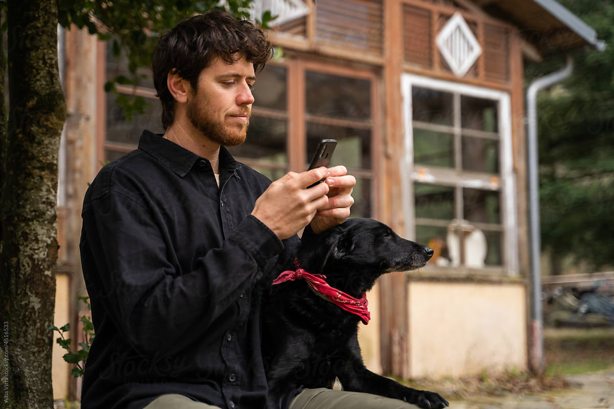 Young man using phone and texting while sitting on bench in the forest