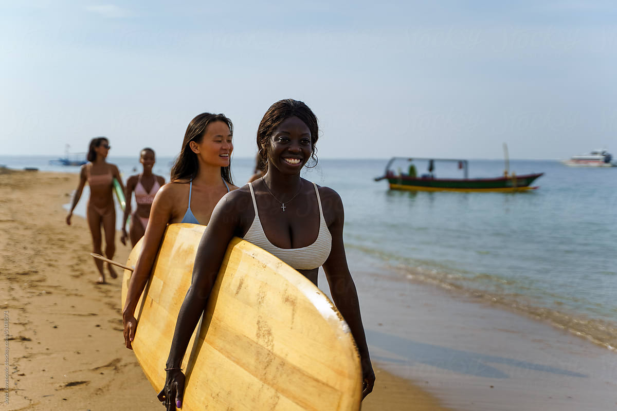 Two women leading group on beach with surfboard