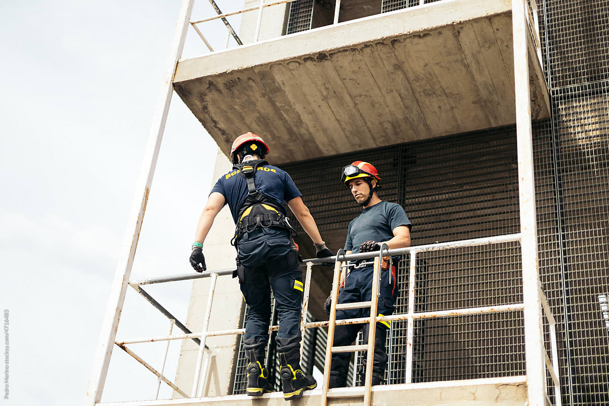 Firefighters climbing a building with a harness and ladder