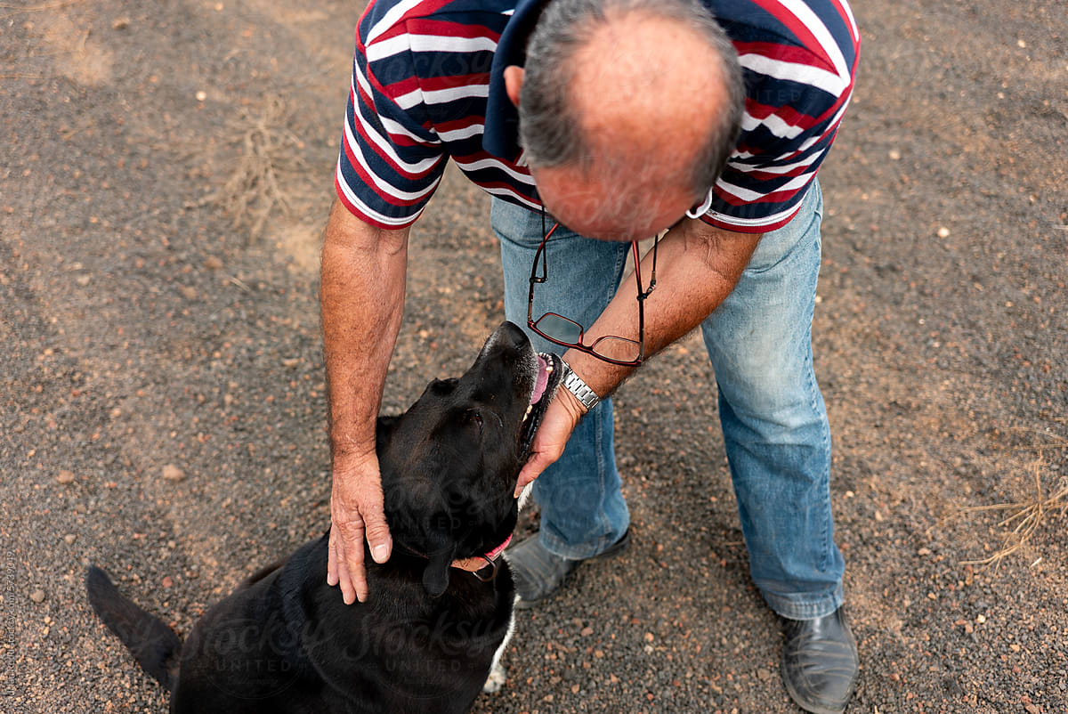 An elderly man bends down to pet his dog