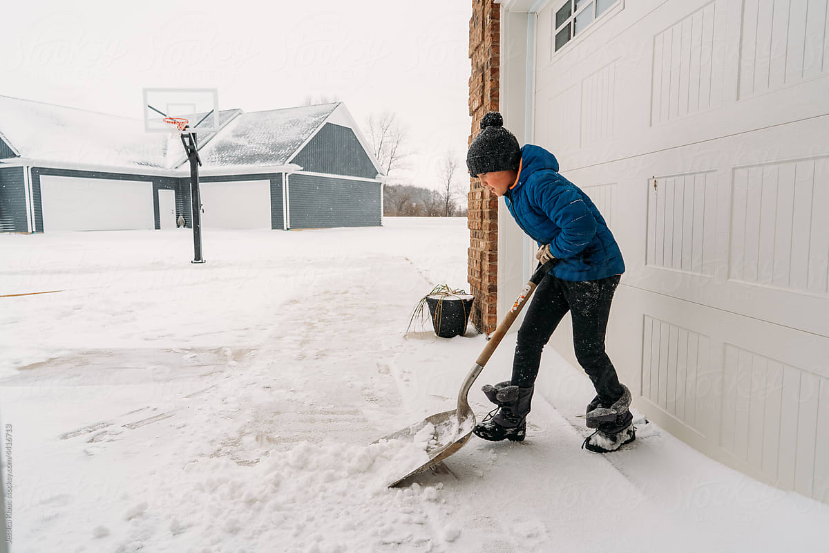 A child pushing a shovel hard to get snow off the ground.