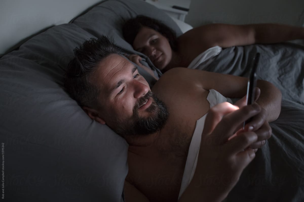 Couple using their phones in bed at night