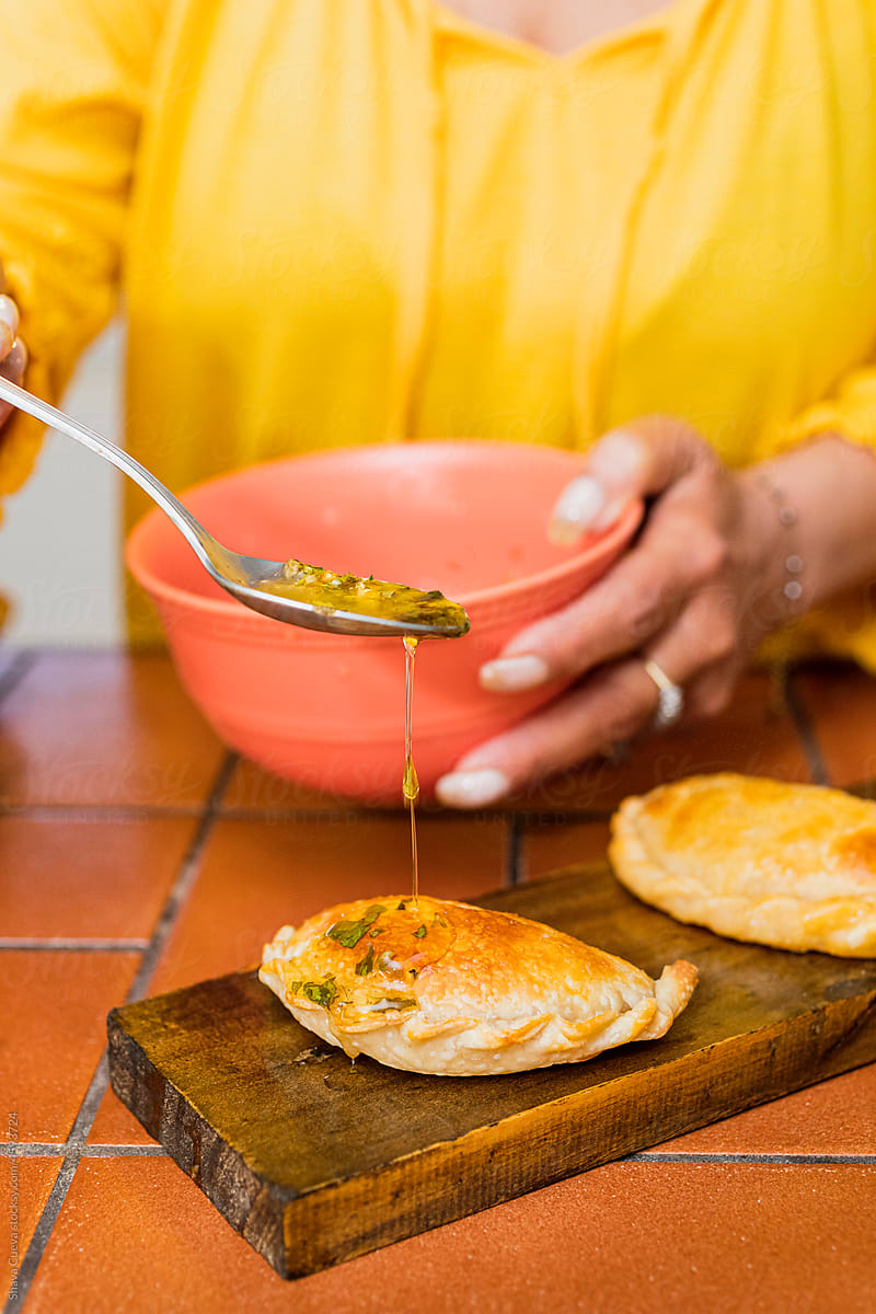 A woman in a yellow shirt putting oil on an Argentinian empanada