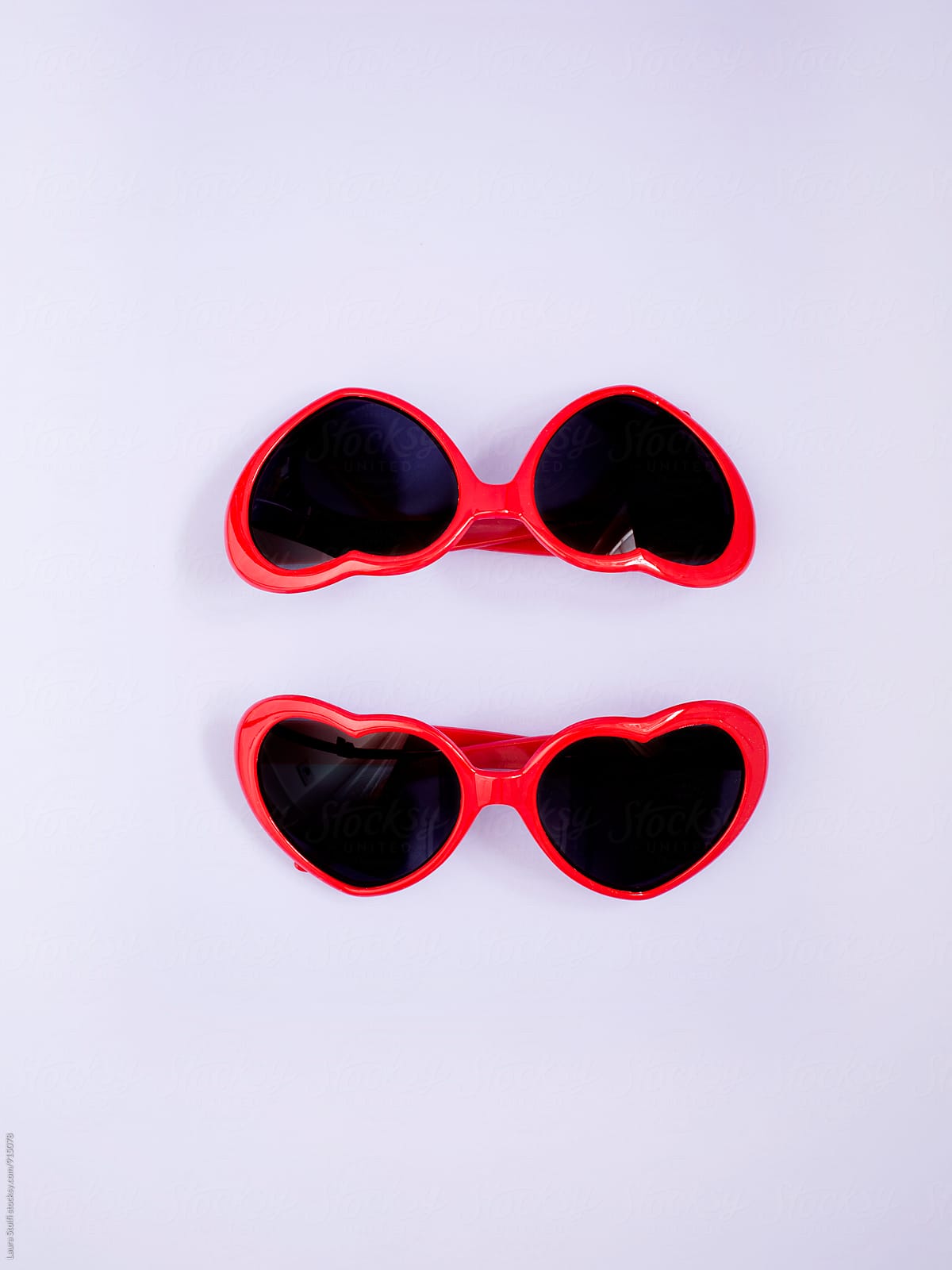Two heart shaped red sunglasses on lilac background