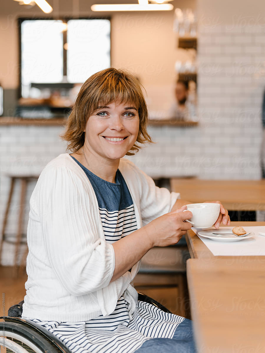 Happy woman using wheelchair having cup of coffee in cafeteria