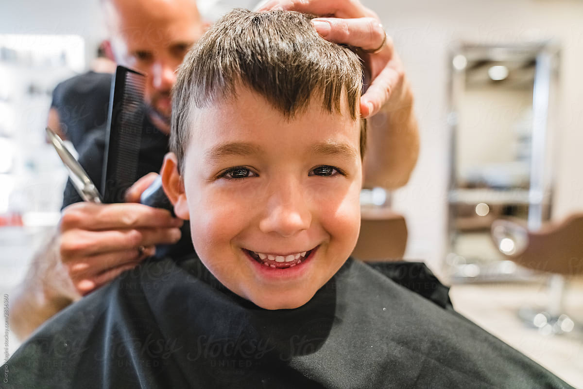 Hairdresser trimming hair of cheerful boy