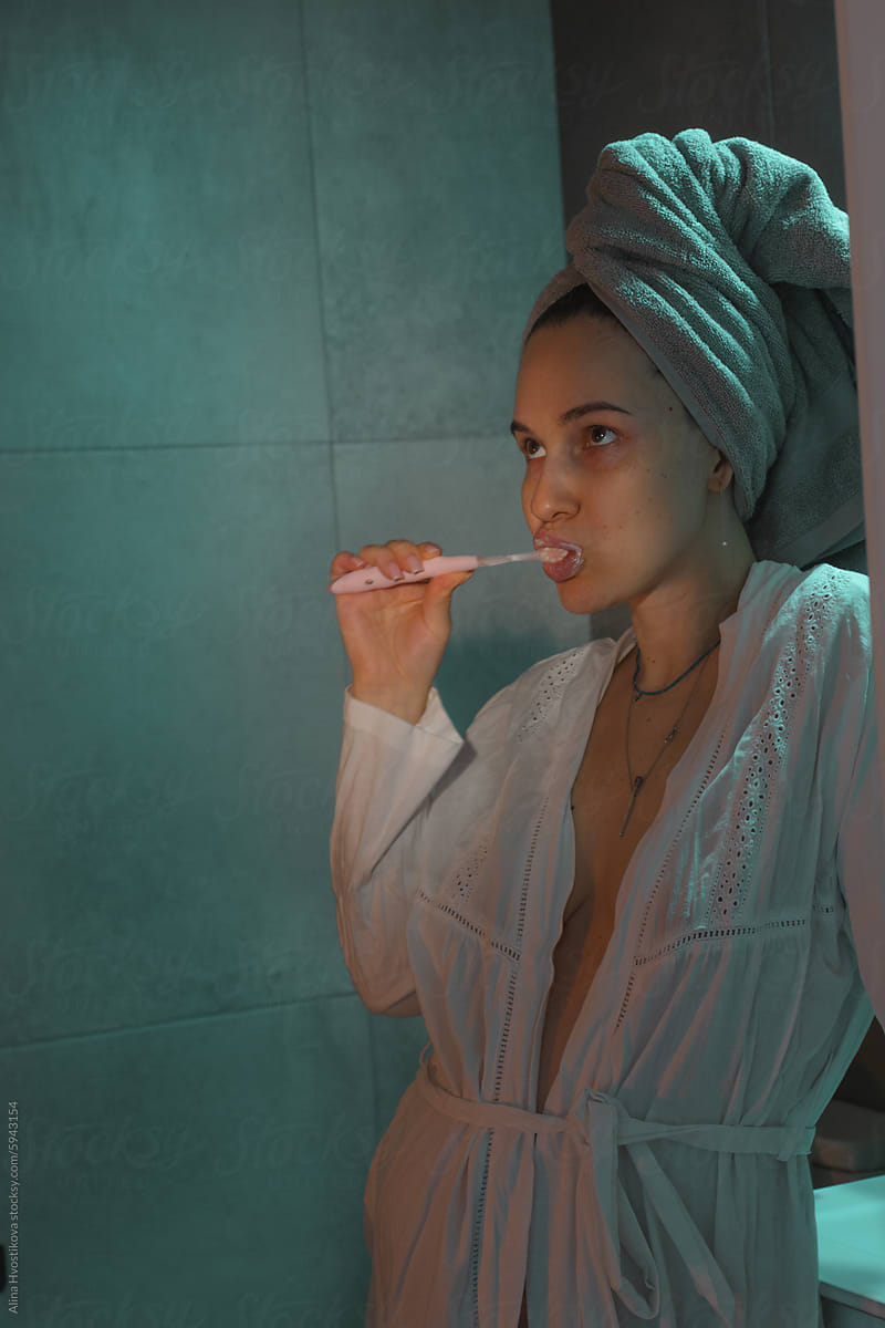 Woman brushing teeth in dark bathroom