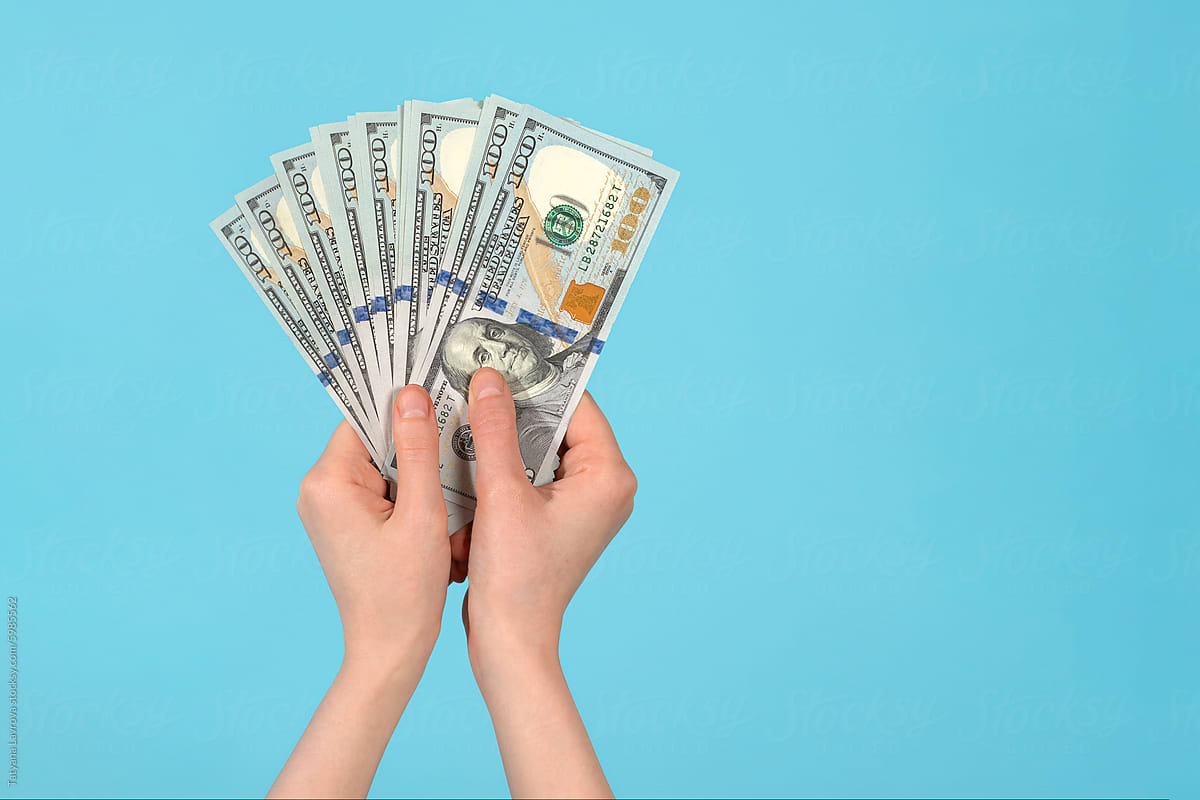Female hand holding one hundred-dollar bills on blue background.
