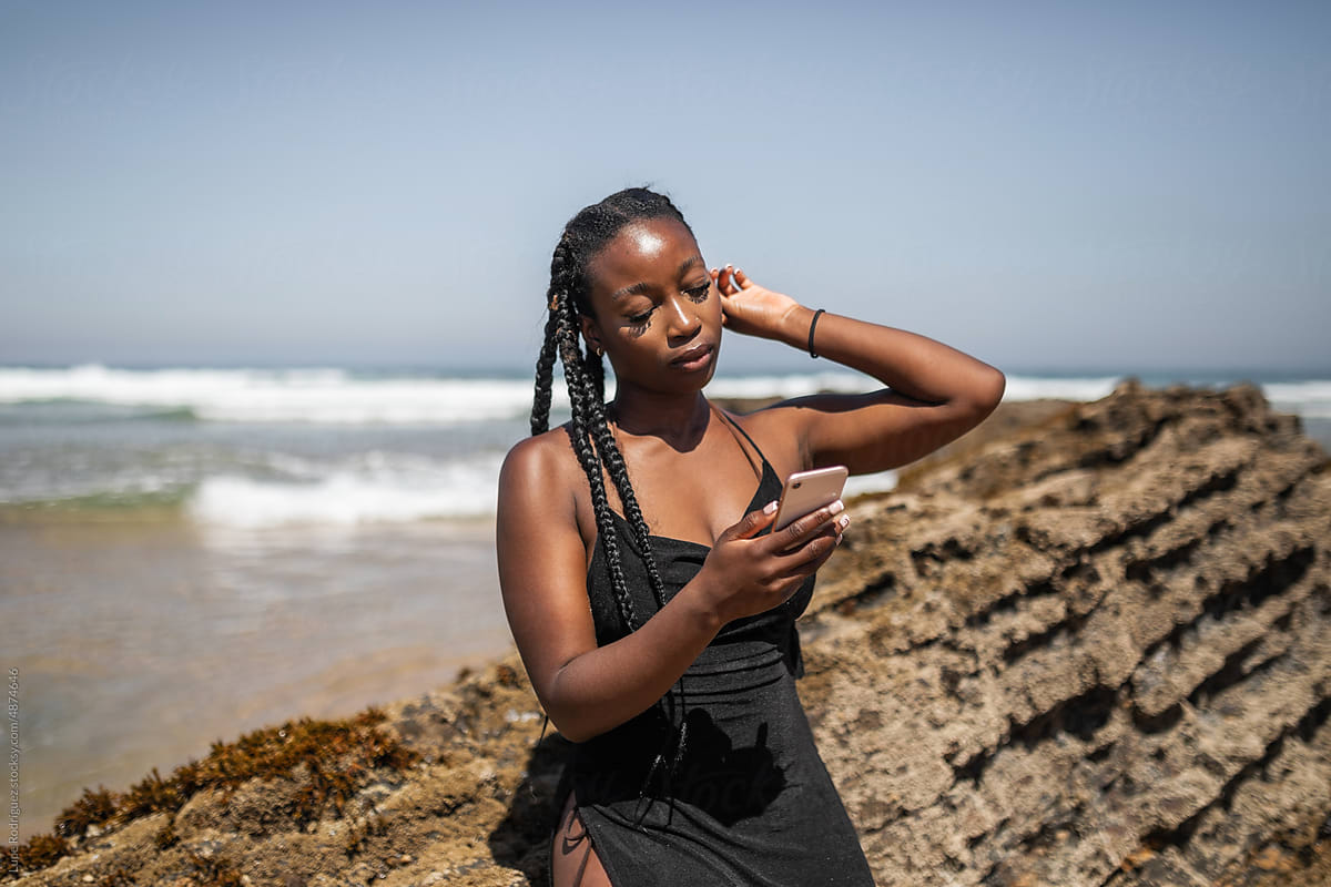 black woman with mobile phone on a beach at the seashore