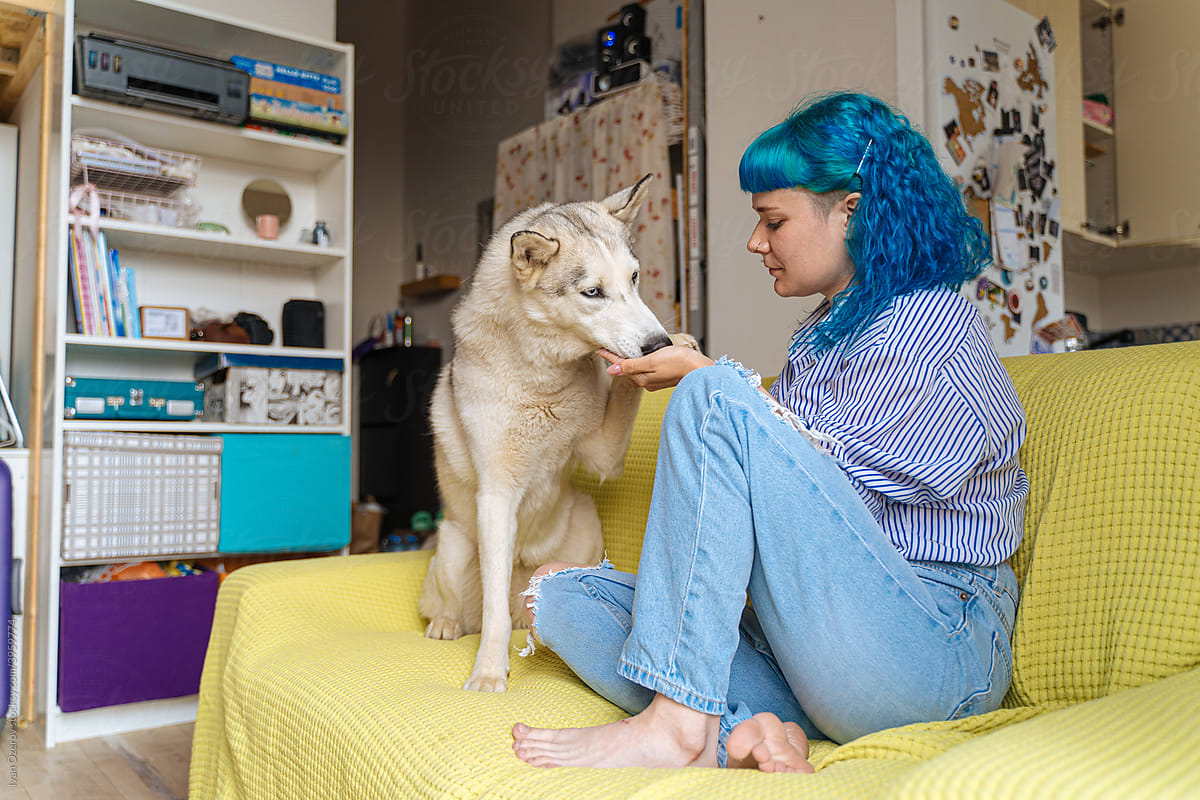 young woman on the couch treats her dog with a snack