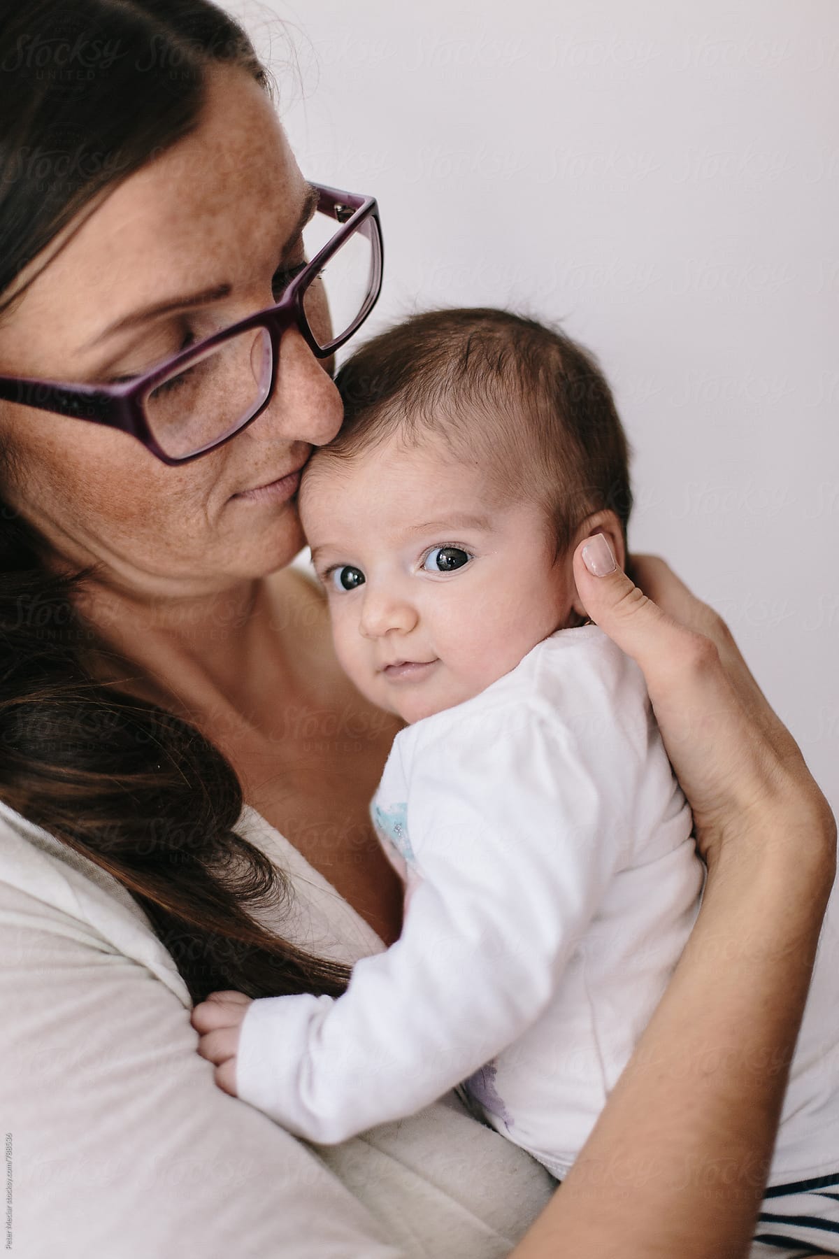Mother Holding Her Little Daughter In Her Arms In Front Of White Wall By Stocksy Contributor 