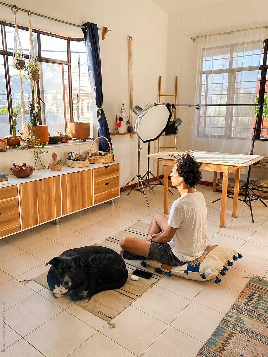 Man meditating on a cushion with his dog in a room