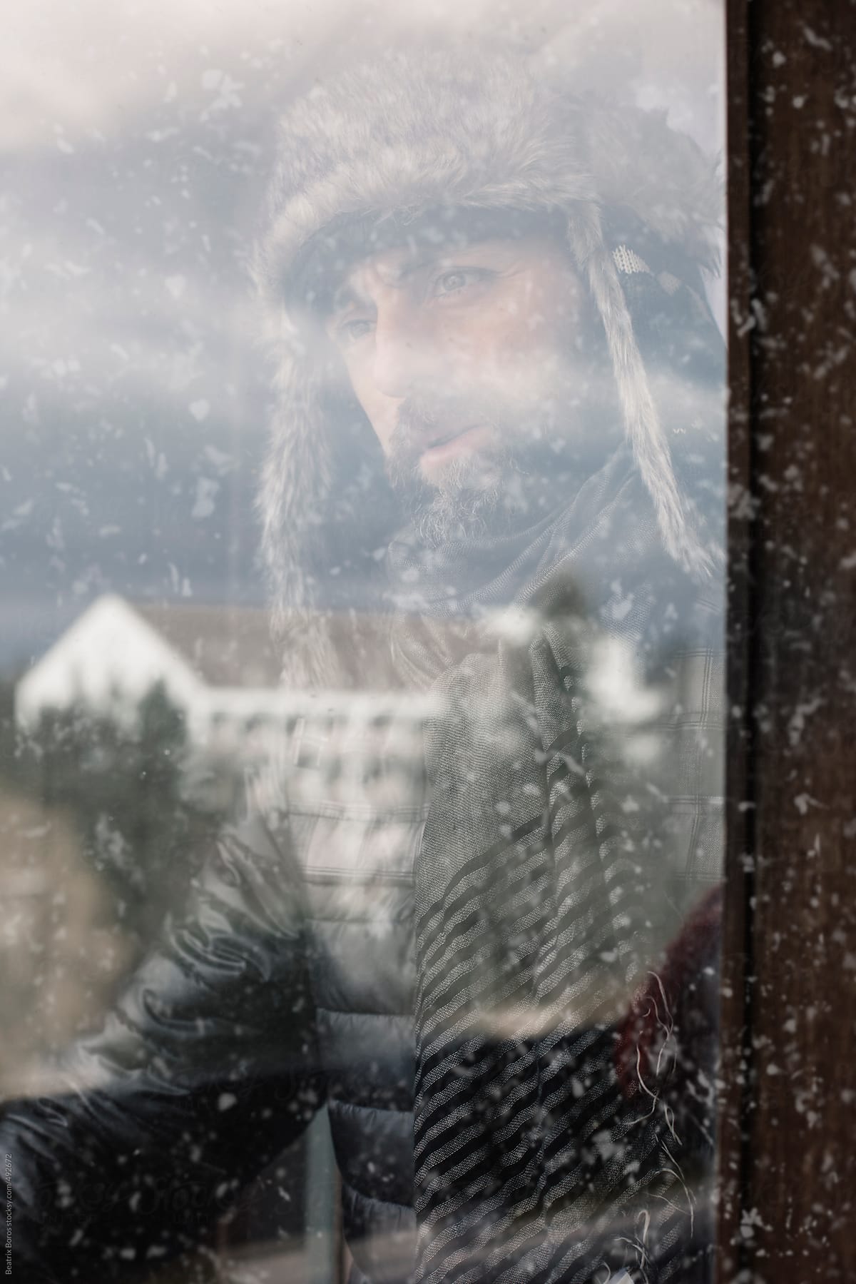 Portrait of a man behind window reflection, wearing winter clothes and hat gazing out of the window