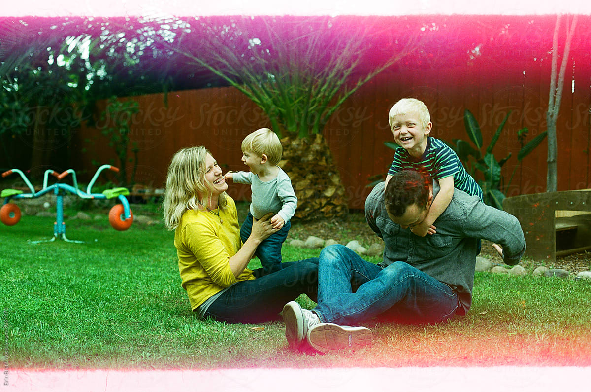 Mom and dad playing with their blond children in the grass in backyard