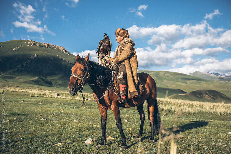 kyrgyz eagle hunter on his horse with a golden eagle in kyrgyz mountain landscape