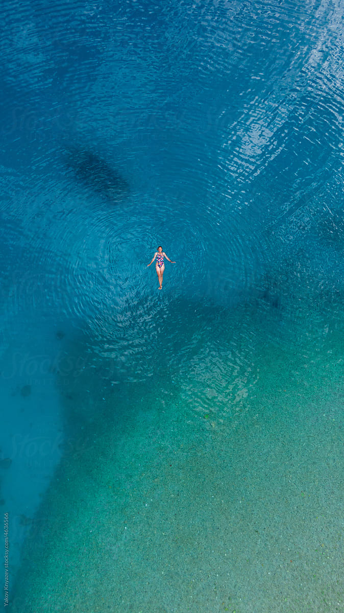 young woman floating in turquoise water, drone overhead