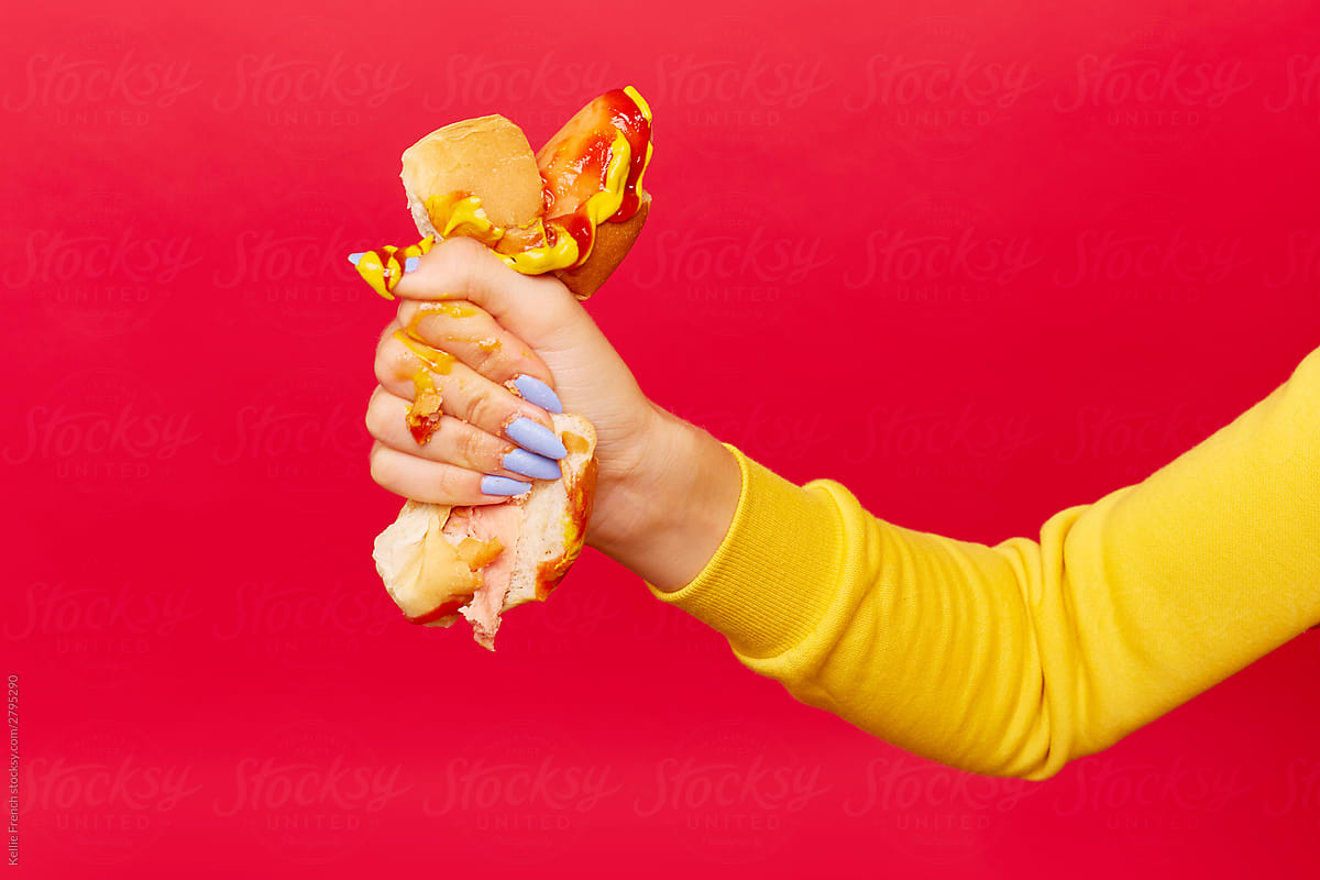 Woman\'s hand with painted blue nails squeezes hotdog