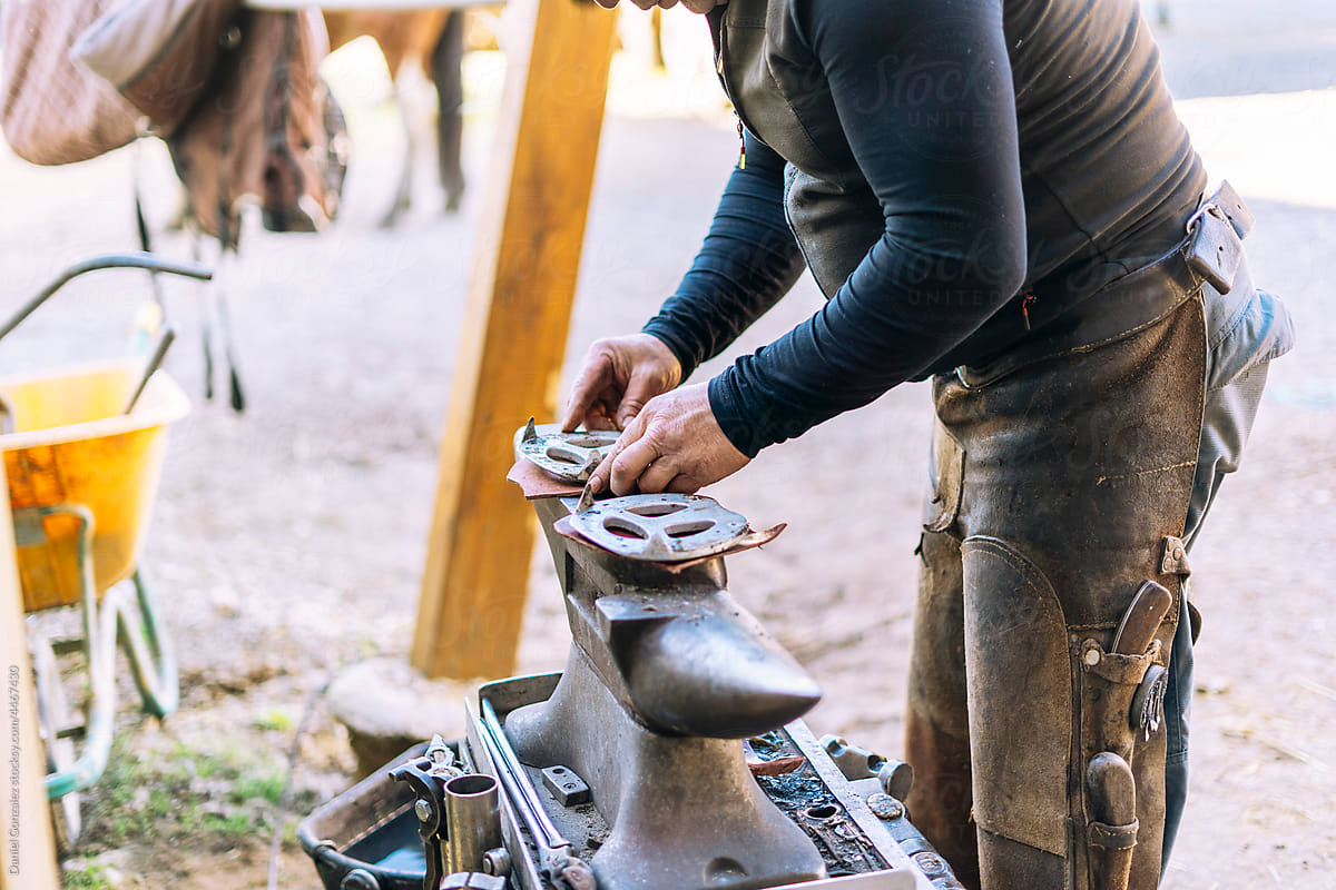 Farrier making iron horseshoes on anvil in stall