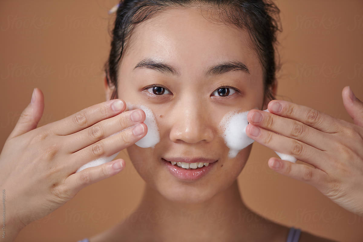 Young asian girl applying cleansing foam cosmetic product on cheeks.