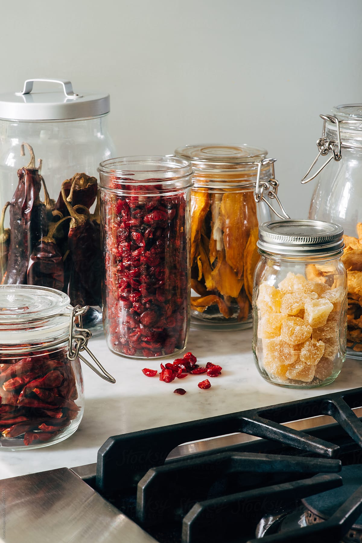 A collection of jar with dried fruits sitting on a counter top next to a stove in a kitchen.