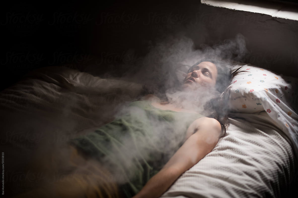 Burning woman lying on bed with surreal smoke