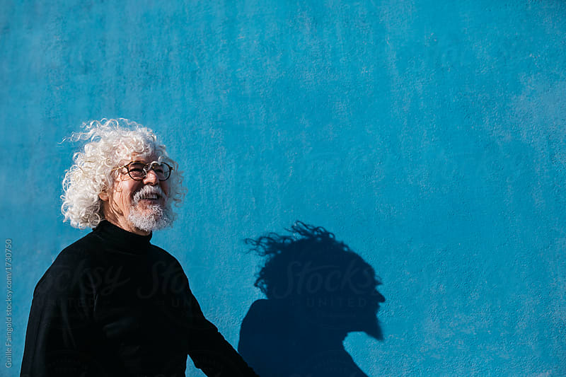 Laughing old hairy man in glasses over blue wall.