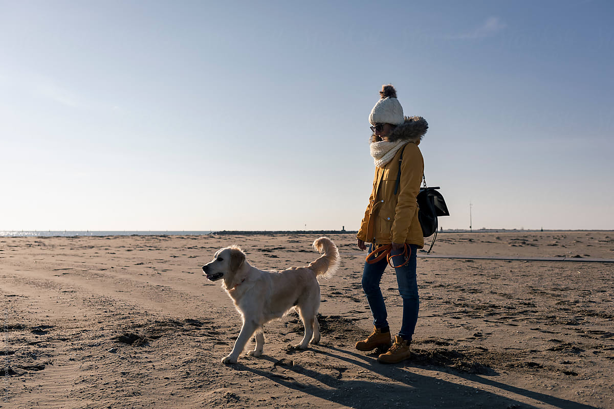 Woman walking with her dog on a beach in winter