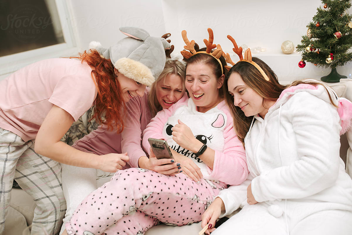 Four Friends Laughing on Sofa in Pajamas with Christmas Antlers.