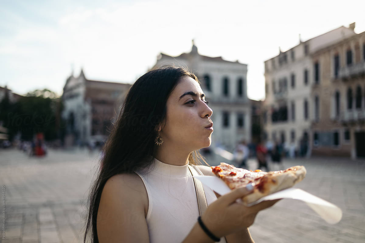 Young woman eating a slice of pizza on the street in Italy