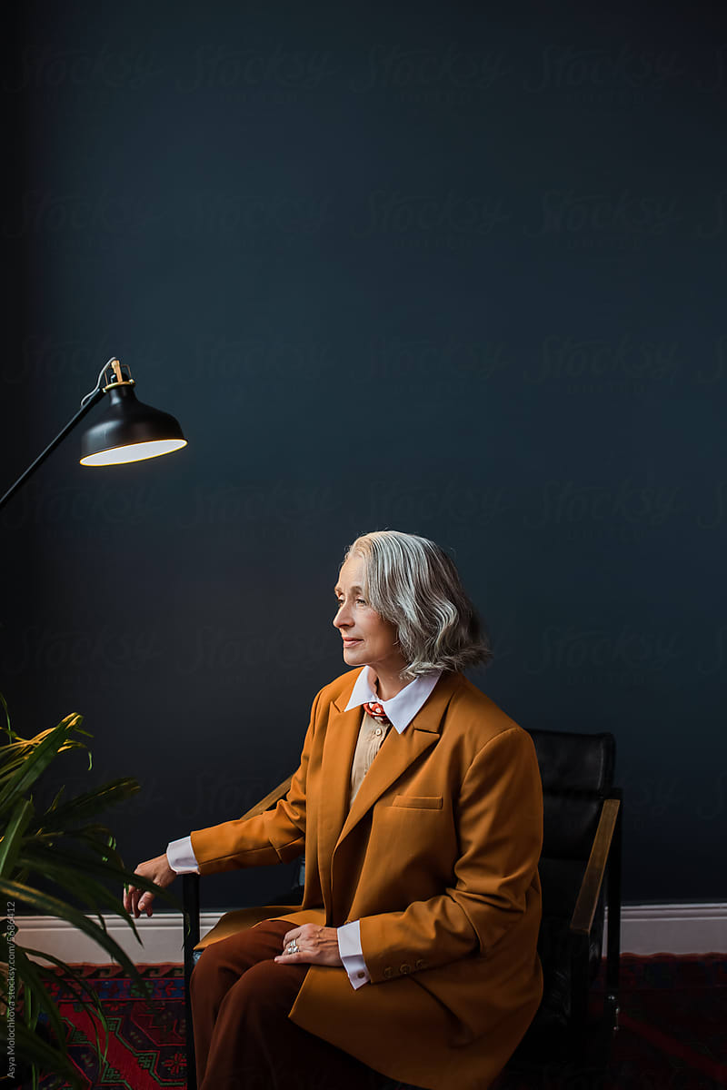 Senior woman sitting on the chair near dark wall