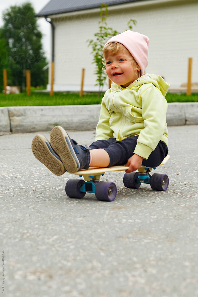 Delighted toddler riding longboard on road