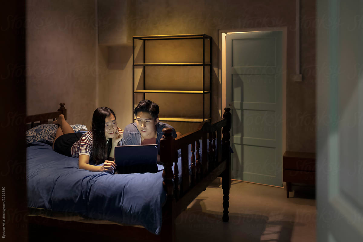 Asian couple on bed watching movies