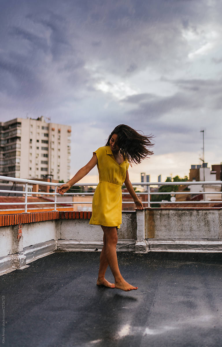 cheerful barefoot woman dancing on rooftop in a rainy day