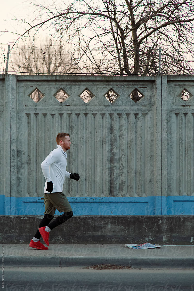 Male athlete running near concrete wall