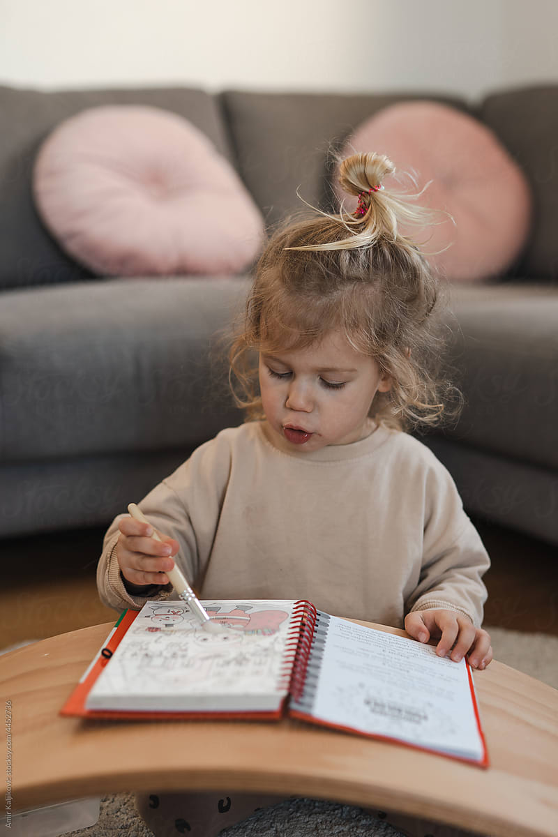 Cute toddler girl painting on a drawing book at home