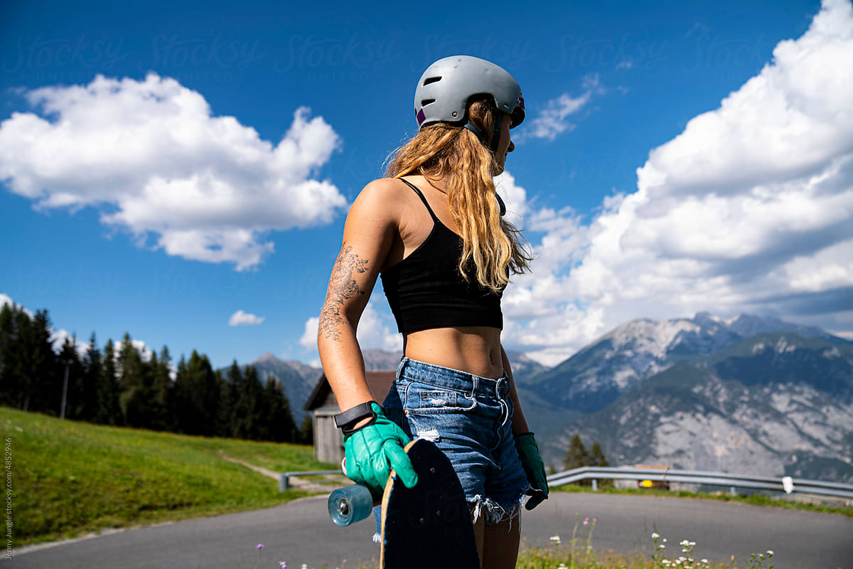 Woman with helmet and skateboard checking the paved road in the alps