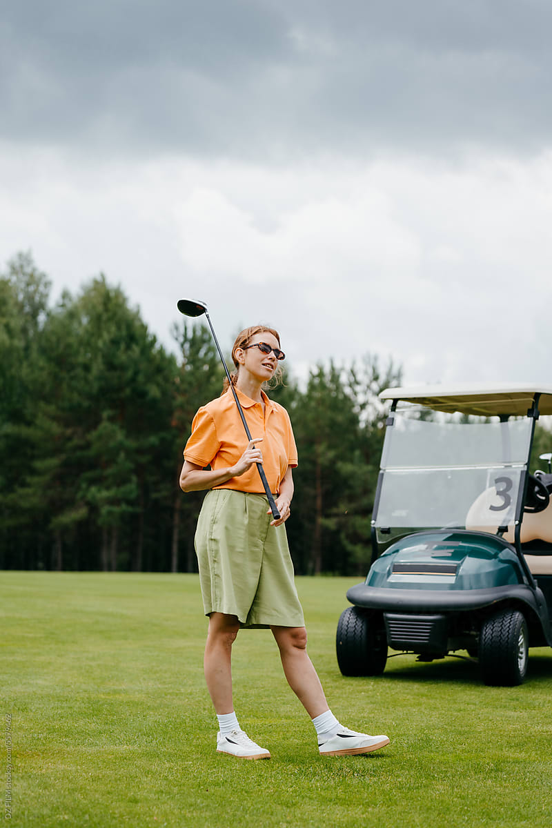 A woman with a golf club stands on a golf court
