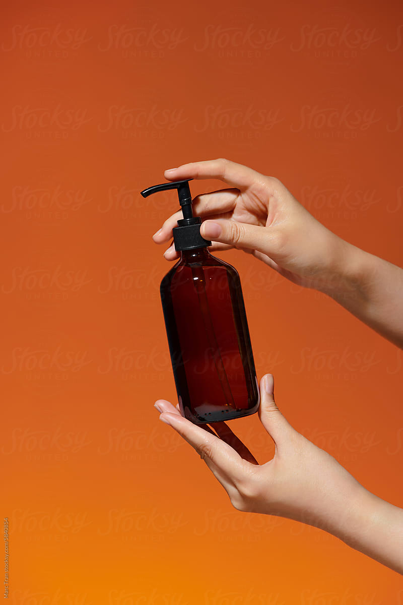 Female hands with amber plastic pump bottle on color background