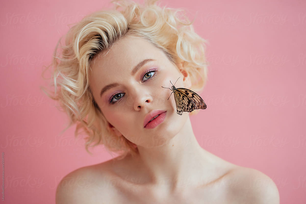 Charming curly blond woman with butterfly sitting on her face